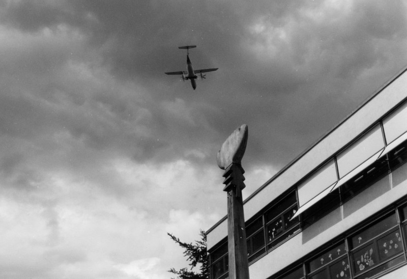 Ein Flugzeug ist zu sehen vor einem Schulgebäude und eine Kunst am Bau Skulptur