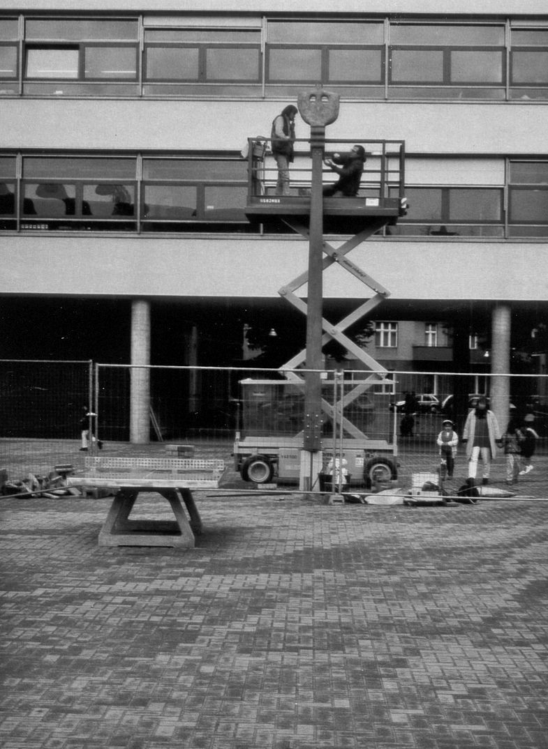 Eine lange Skulptur wird montiert, 2 Personen helfen mit und 4 Personen schauen