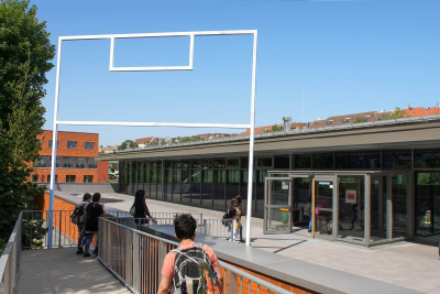 Weißer Metallrahmen in Spielfeldform als Tor über dem Eingang einer Sporthalle.