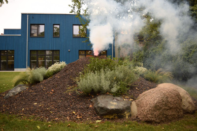 Vulkan aus Lavagestein mit Rauch und blauen Haus im Hintergrund