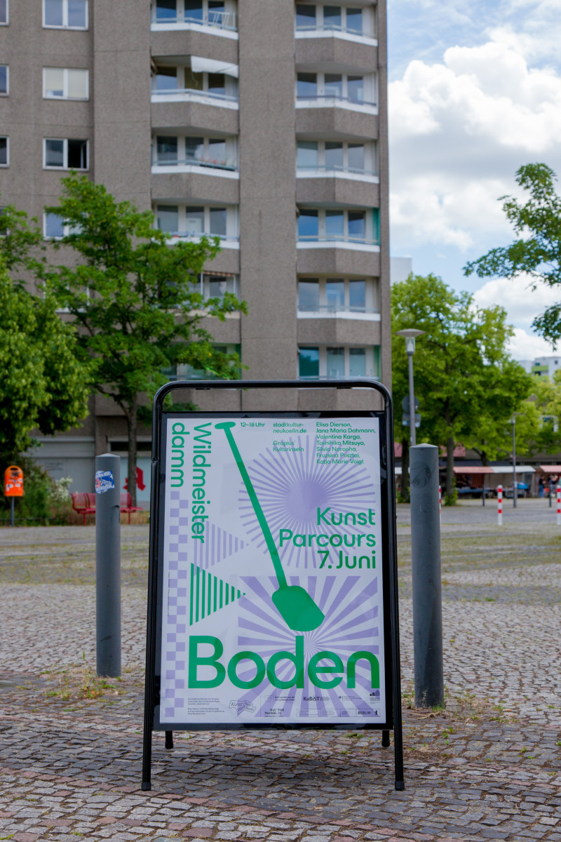 text: >
  Plakat für Kunstparcours Boden am 7.
  Juni in Neukölln mit grünem
  Spaten-Symbol auf abstraktem violettem
  Hintergrund, aufgestellt auf einem Platz
  vor einem Wohngebäude
decorative: false
source: manual