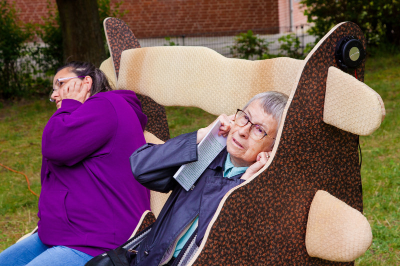text: >
  Zwei Personen sitzen in der übergroßen
  Kunstskulptur „Head rest