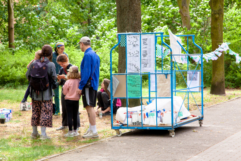 text: 'Gruppe von Kindern und Erwachsenen betrachtet ein blaues Ausstellungsgerüst mit ausgehängten Zeichnungen im Rahmen des Workshops Boden-Probe(n) – Playing in the Dirt  von Jana Maria Dohmann und Fruzsina Pusztai im Park'
decorative: false
source: reviewed