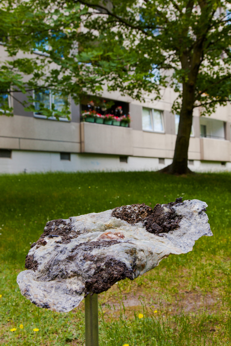 text: 'Silvia Noronhas Installation Shifting Geologies: graubraunes geologisches fragment auf Pfahl vor modernem Wohngebäude unter blühendem Baum'
decorative: false
source: reviewed