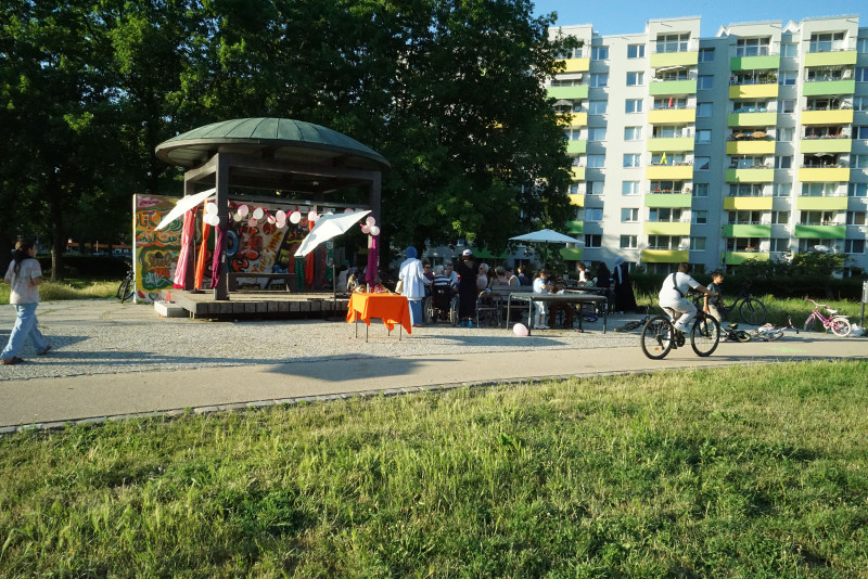 text: >
  Pavillon auf öffentlichem Platz vor
  Wohnblöcken, umgeben von Besuchern und
  Fahrradfahrern
decorative: false
source: reviewed