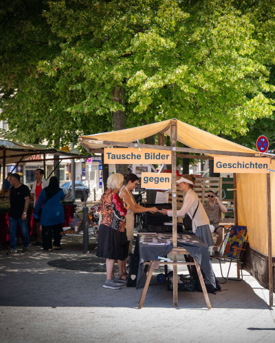 Marktstand mit Holzkonstruktion, an dem Künstlerin Petra Spielhagen Besucher*innen einlädt, Bilder gegen Geschichten zu tauschen
