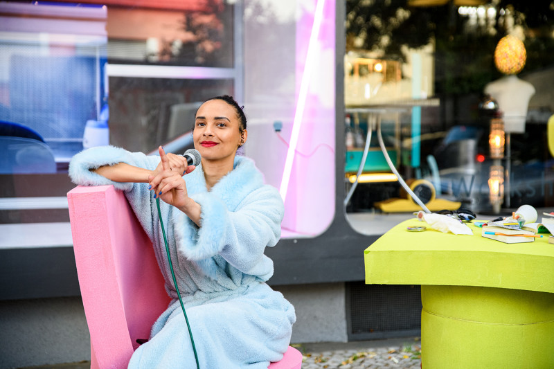 text: >
  Frau mit Mikrofon und Bademantel in der
  Straße
decorative: false
source: manual