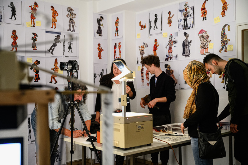 text: >
  Fünf Menschen sind gesamelt in einem
  Raum mit Bildern auf die Wand
decorative: false
source: manual